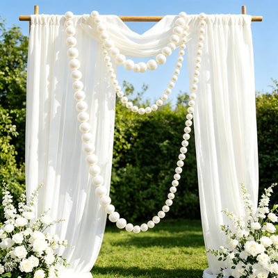 Elegant outdoor wedding arch with white drapery and pearl garlands
