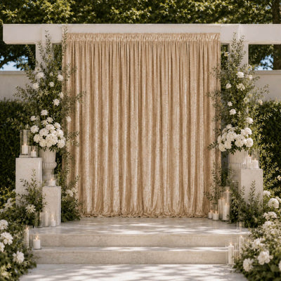 Elegant outdoor wedding backdrop with gold drapes, white flowers, and candles