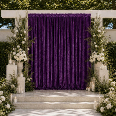 Elegant outdoor wedding backdrop with purple drapery, white flowers, and candles