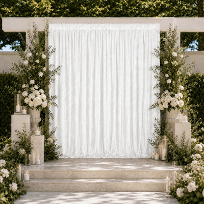 Elegant outdoor wedding ceremony arch with white drapery, flowers, and candles