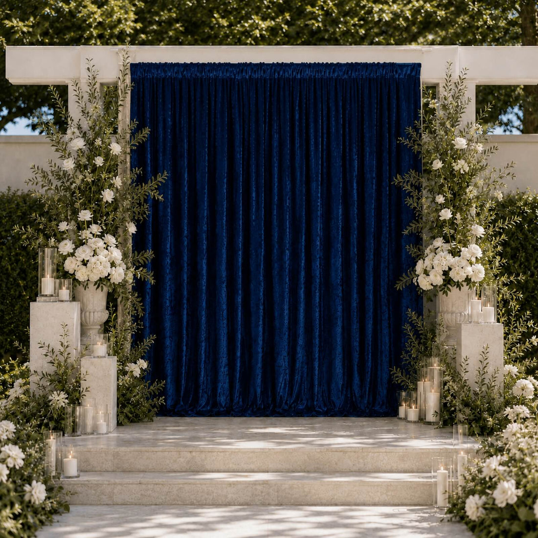 Elegant outdoor wedding ceremony backdrop with blue drape, white flowers, and candles
