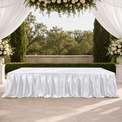 Elegant outdoor wedding reception table with white satin tablecloth and floral drapery