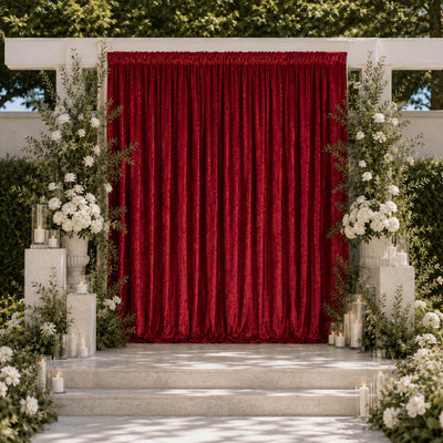 Elegant outdoor wedding stage with red velvet curtains, white flowers, and candles