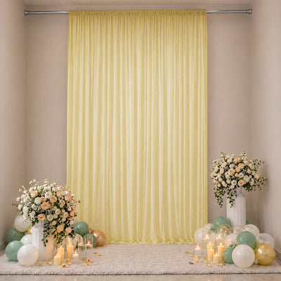 Elegant pastel party backdrop with yellow drape, flowers, candles, and balloons