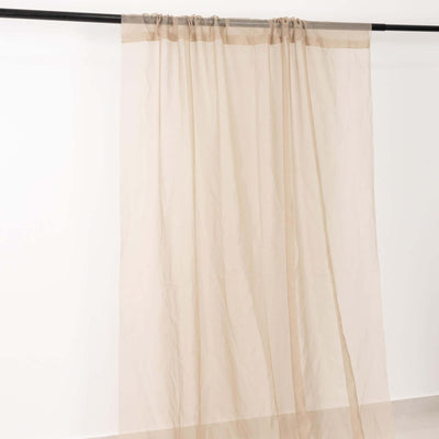 Sheer beige curtain draped on a rod against a plain backdrop