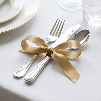 Elegant silver flatware tied with gold ribbon on a white table setting