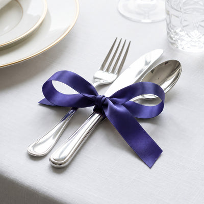 Elegant table setting with purple ribbon-tied silverware on white linen tablecloth
