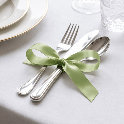 Elegant table setting with silver cutlery tied with a green ribbon on white linen tablecloth