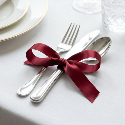 Elegant table setting with silverware tied by burgundy ribbon on white linen