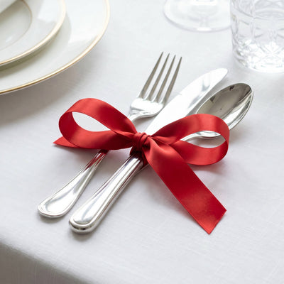 Elegant table setting with silverware tied in a red ribbon on white linen tablecloth
