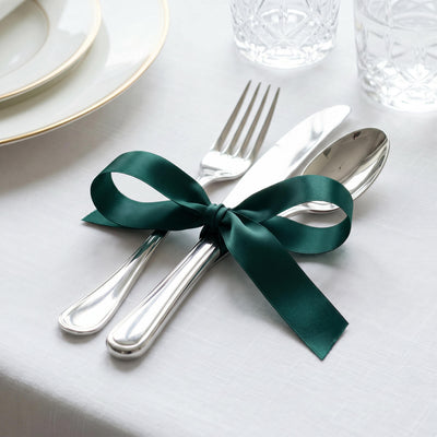 Elegant table setting with silverware tied with dark green ribbon on white linen
