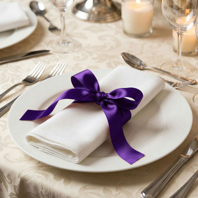 Elegant table setting with white napkin and purple ribbon bow on plate