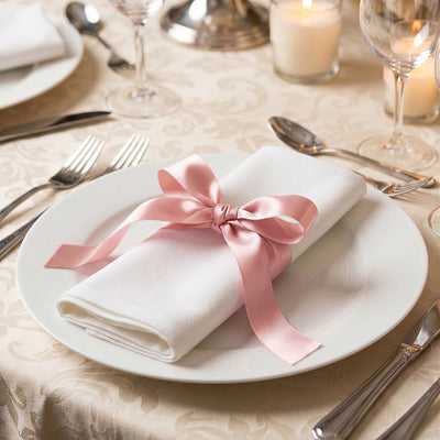 Elegant table setting with white plate, pink ribbon napkin, and candles