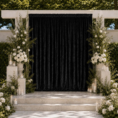 Elegant wedding ceremony backdrop with black drape, white flowers, and candles