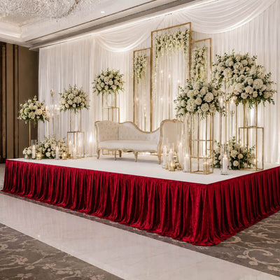 Elegant wedding stage décor with white flowers, gold accents, and red velvet skirting