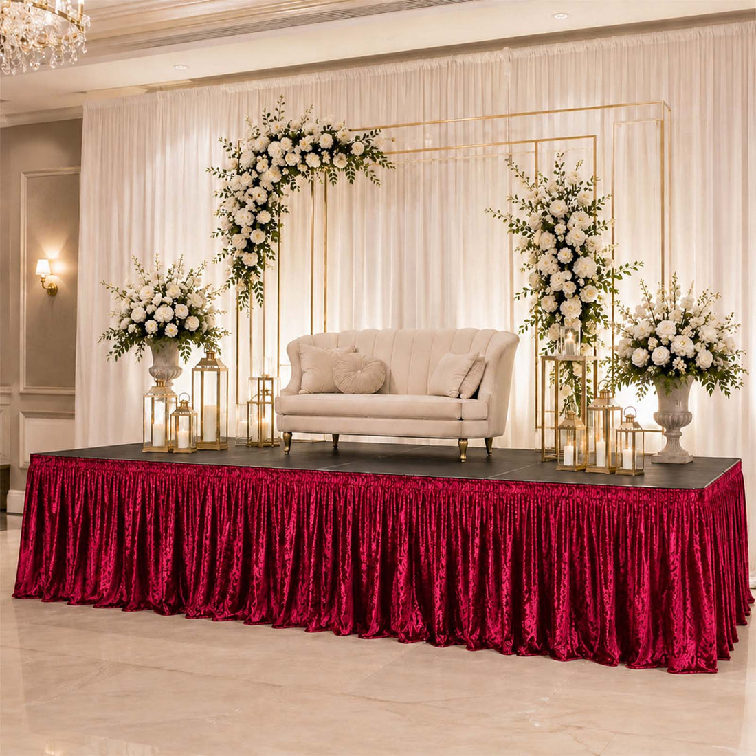 Elegant wedding stage with floral arch, cream loveseat, and red velvet drape