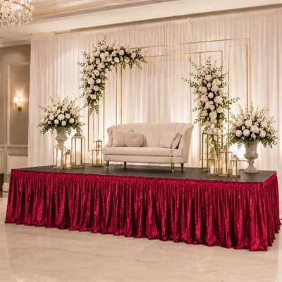 Elegant wedding stage with floral arch, cream loveseat, and red velvet drape