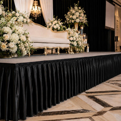 Elegant wedding stage with floral arrangements and gold sofa on black draped platform