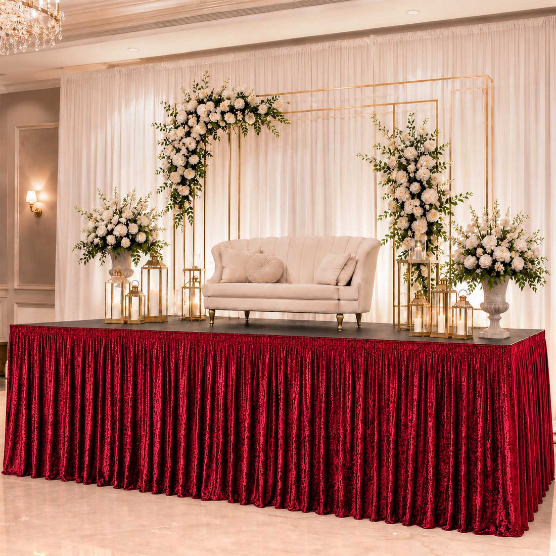Elegant wedding stage with floral backdrop, cream loveseat, and red velvet table skirt