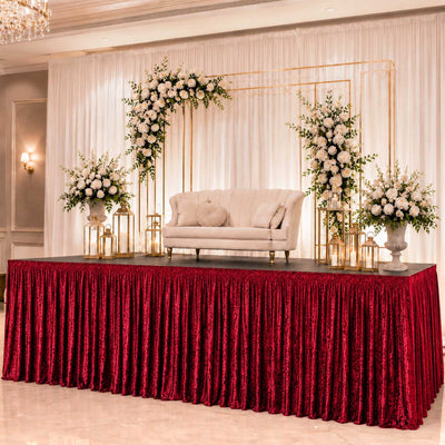Elegant wedding stage with floral backdrop, cream loveseat, and red velvet table skirt
