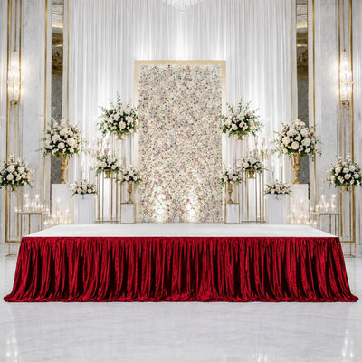 Elegant wedding stage with floral backdrop, gold accents, and red velvet table skirt