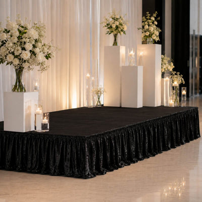 Elegant wedding stage with white floral arrangements and candles on black draped platform