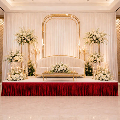 Elegant wedding stage with white floral decor, gold arch, and velvet red drape