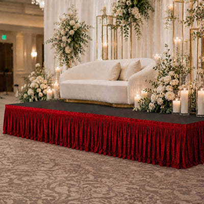 Elegant wedding stage with white sofa, candles, and floral decor on red velvet skirting