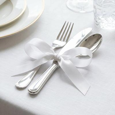 Elegant white ribbon tied around silver cutlery on a formal table setting