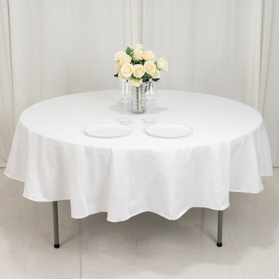 Round table set with white tablecloth, plates, and a vase of roses.
