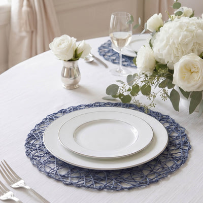 Elegant white table setting with blue woven placemats, roses, and glassware