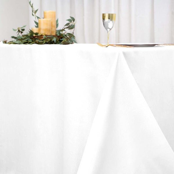 Elegant white tablecloth with gold-accented glassware and candles for dining setup.