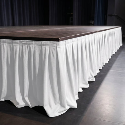 Empty event stage with dark wood platform and white pleated skirt table cover