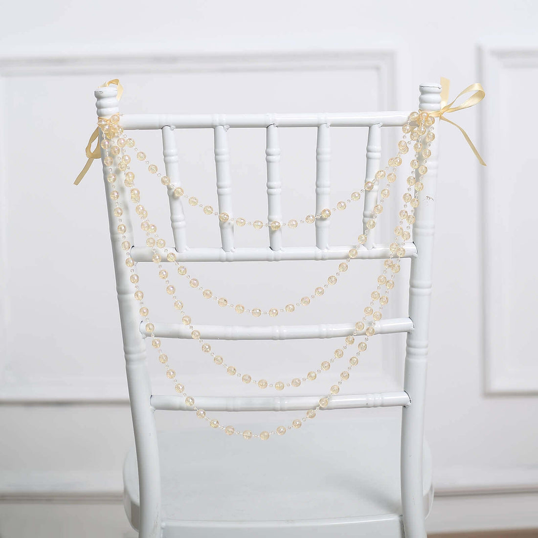 Decorative yellow bead garland draped over a white chiavari chair.