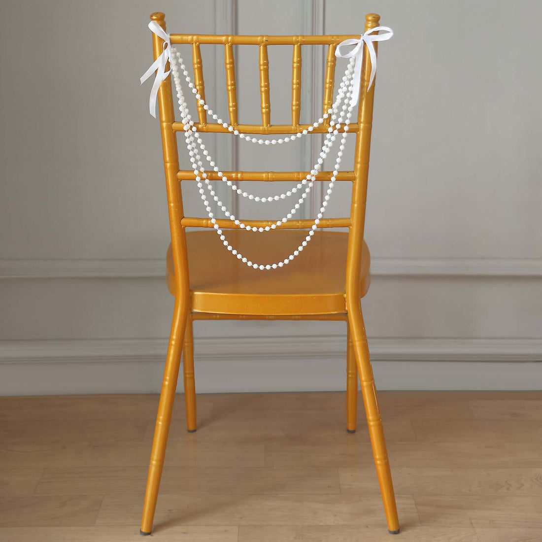 Gold chiavari chair adorned with white pearl garland and ribbons.