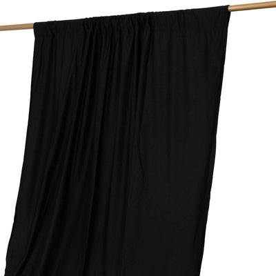 Black curtain draped on a wooden rod against a white backdrop.