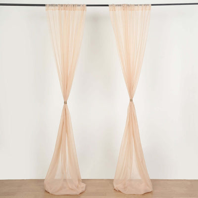 Sheer peach curtain panels hanging on a rod against a plain backdrop.