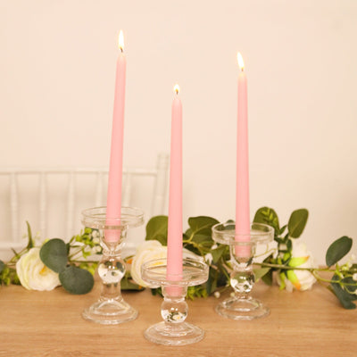 Pink taper candles in clear glass holders with greenery and roses.