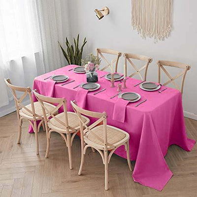 Pink tablecloth on a dining table set with plates and chairs in a bright room.