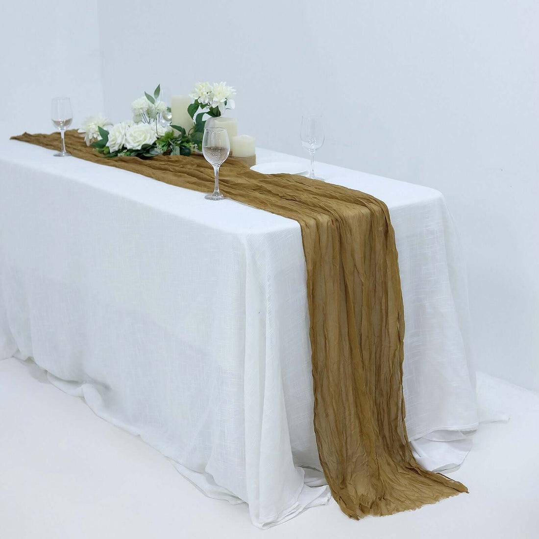 Elegant gold table runner with flowers and candles on a white table.