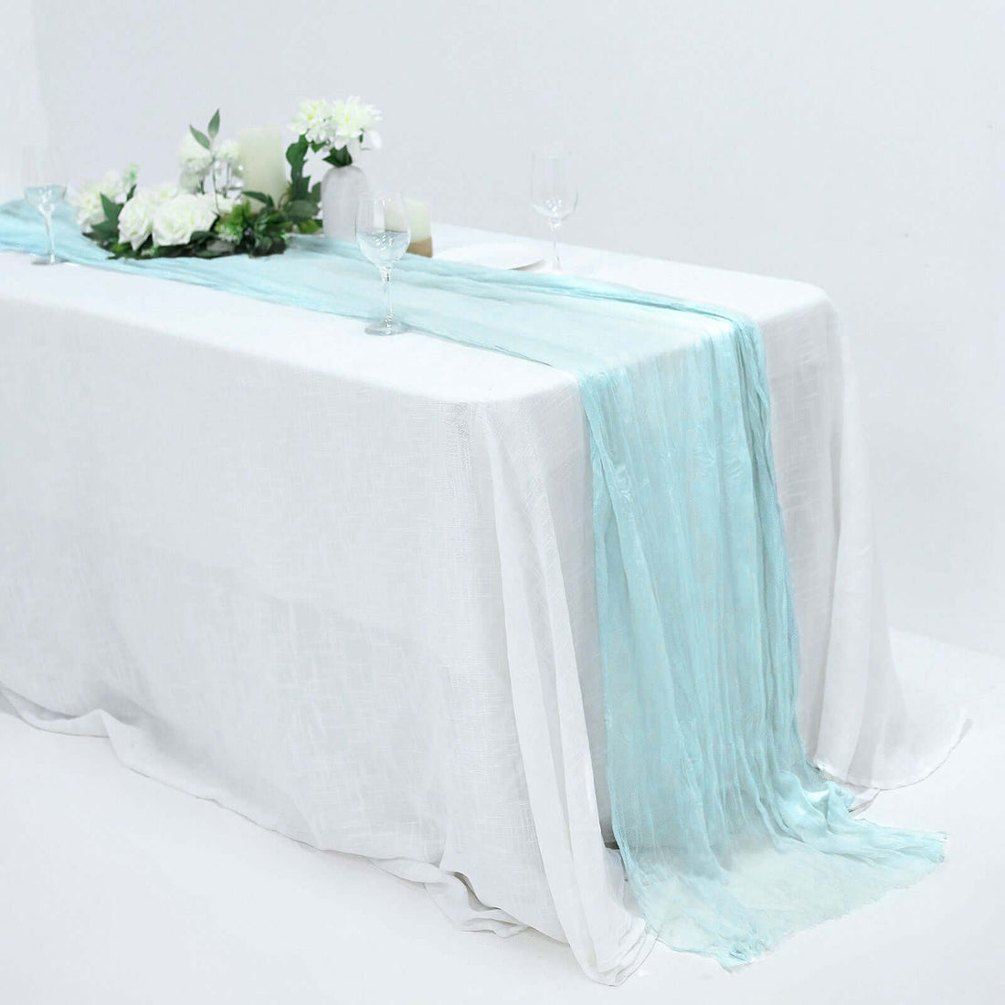 Elegant aqua table runner on a white table with floral decor and glassware.