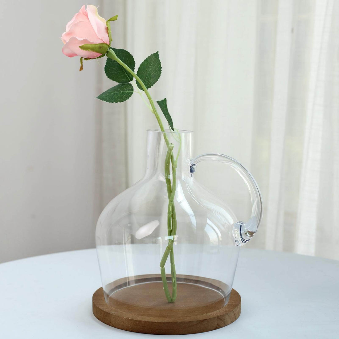 Clear glass vase with pink rose, displayed on a wooden base.