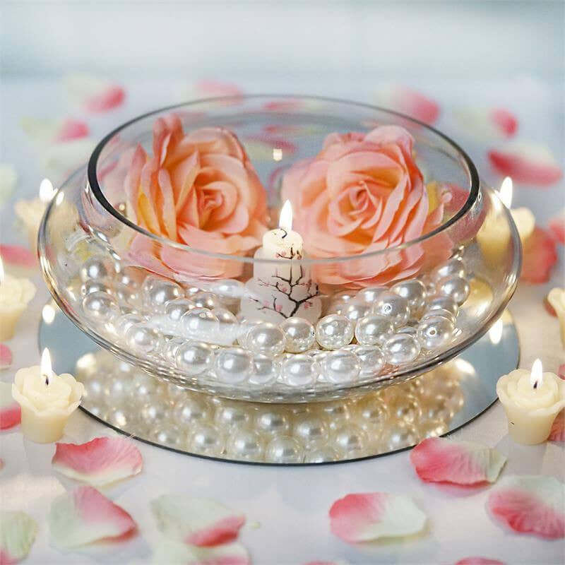 Decorative glass bowl with roses, pearls, and candles on a mirrored base.