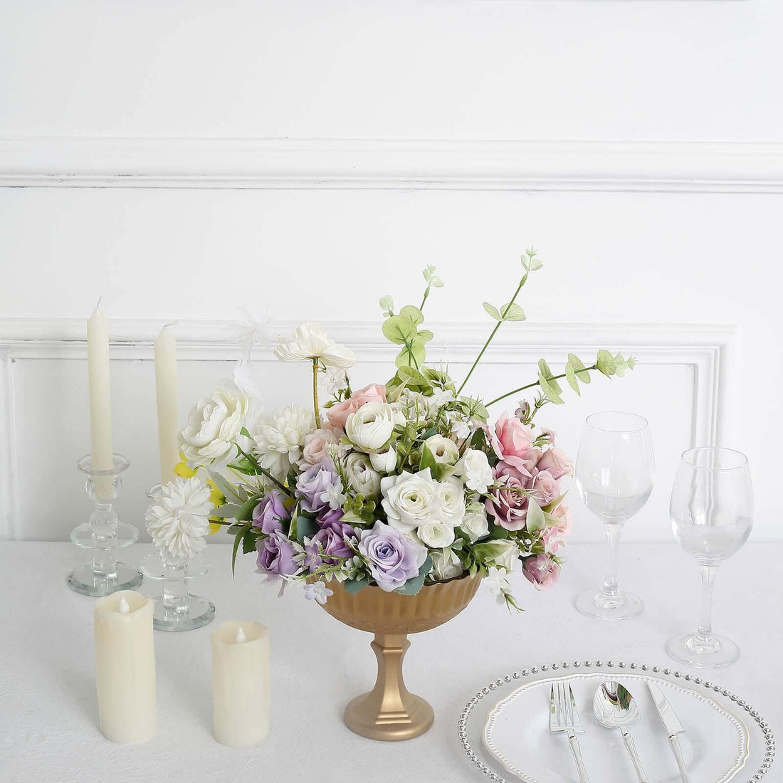 Elegant floral arrangement in a gold vase with candles and tableware