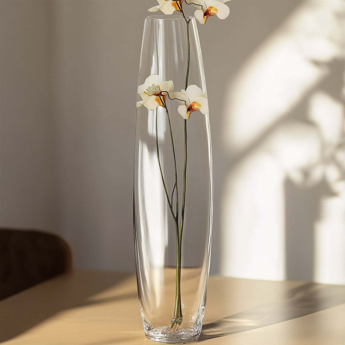 Tall glass vase with white flowers, casting soft shadows.