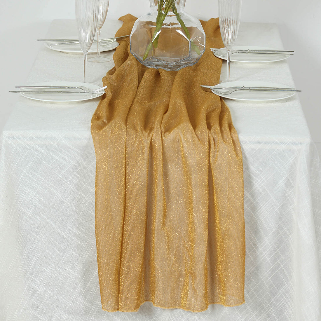 Gold table runner draped elegantly on a white tablecloth with clear dinnerware.
