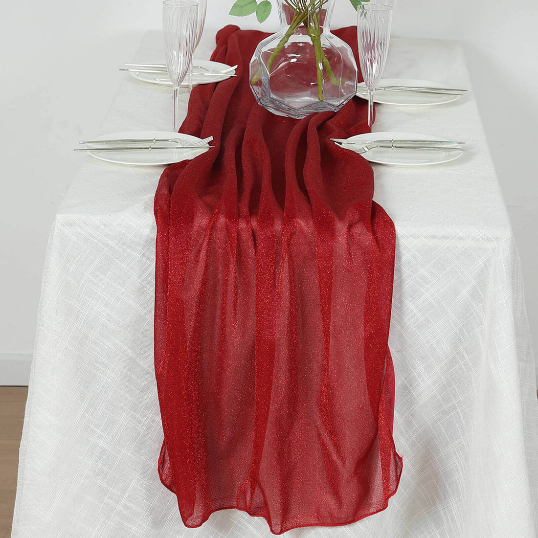 Red sheer table runner draped elegantly on a white tablecloth.