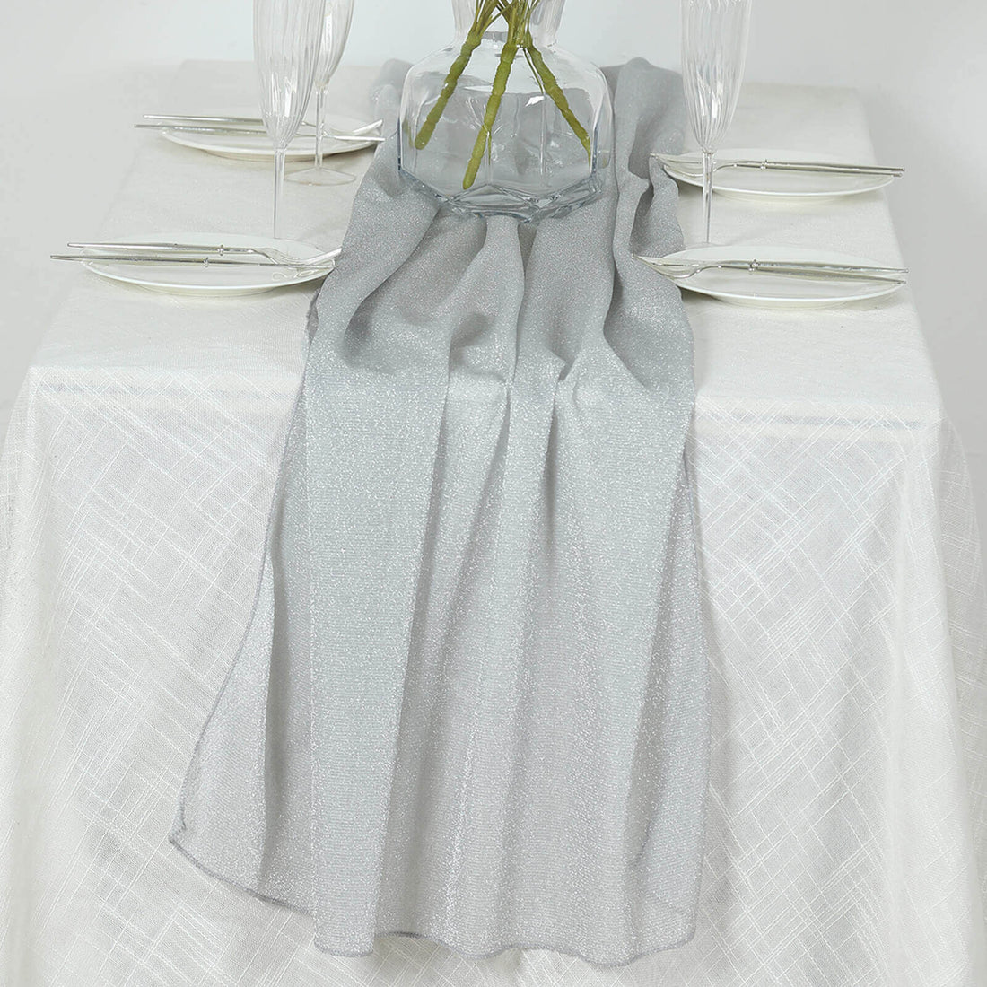 Silver table runner on a white table with elegant glassware and floral decor.