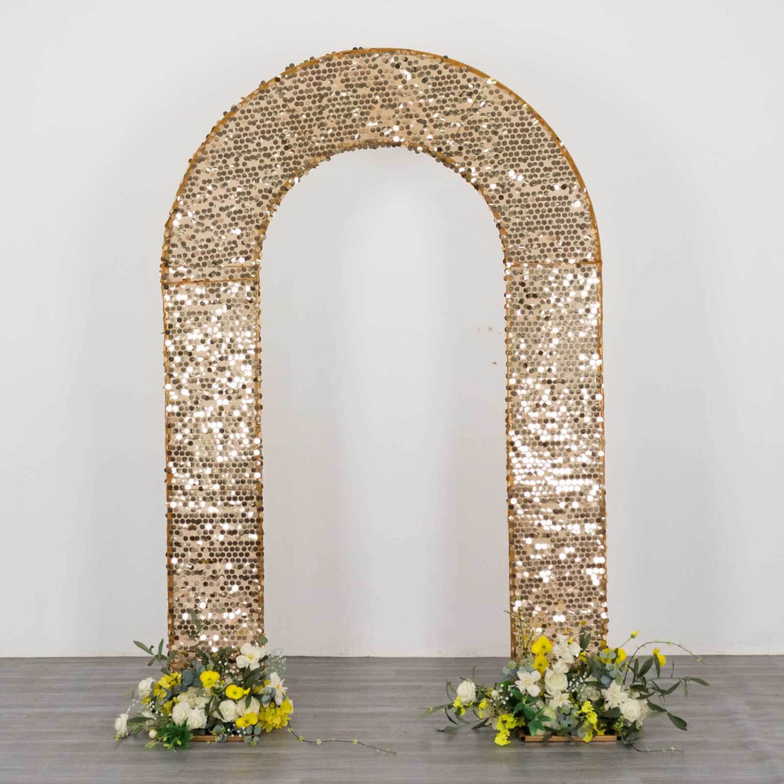 Gold sequin wedding backdrop arch with floral arrangements on the base.