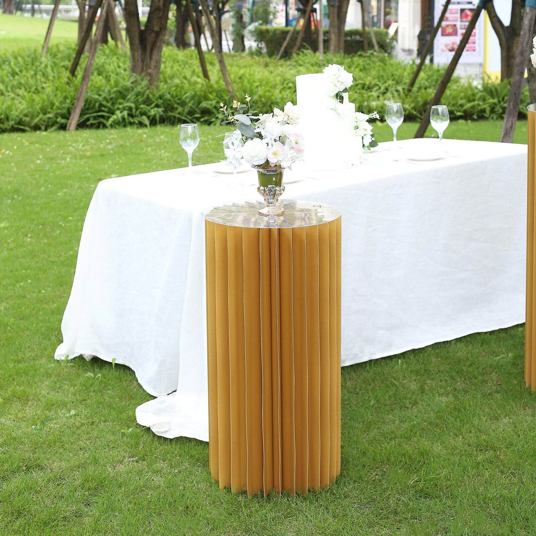 Stylish round gold table with pleated design, set in an outdoor event setting.